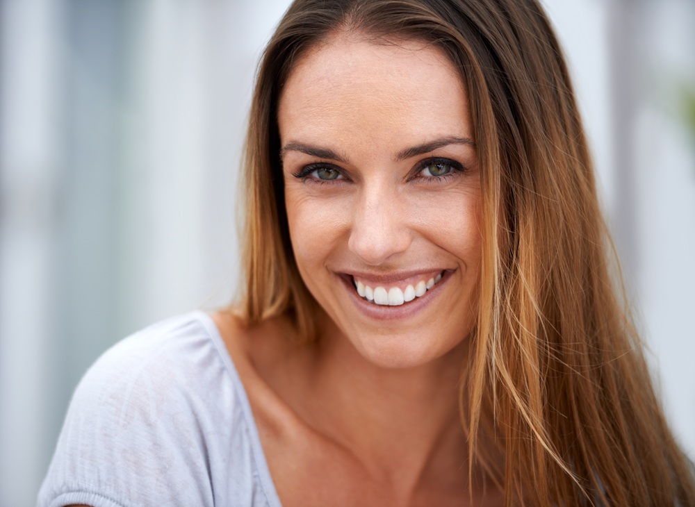 Close-up of a cheerful woman with long brown hair and a radiant smile, representing relief and confidence – TMJ Specialist San Diego